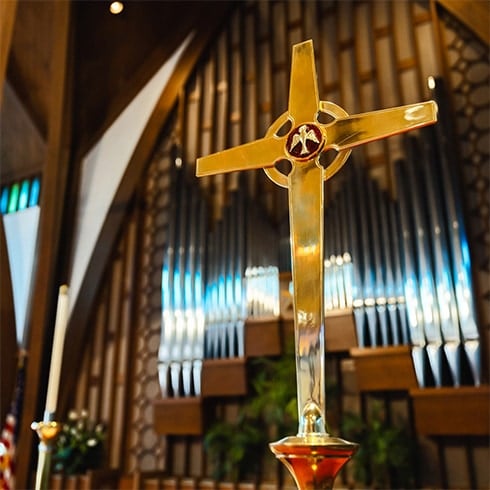A church cross surrounded by a pipe organ in the background.